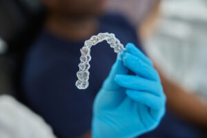 Alineador Invisalign transparente en una clínica dental en Castellón, sostenido por un dentista con guantes azules. Ortodoncia invisible para una sonrisa perfecta.